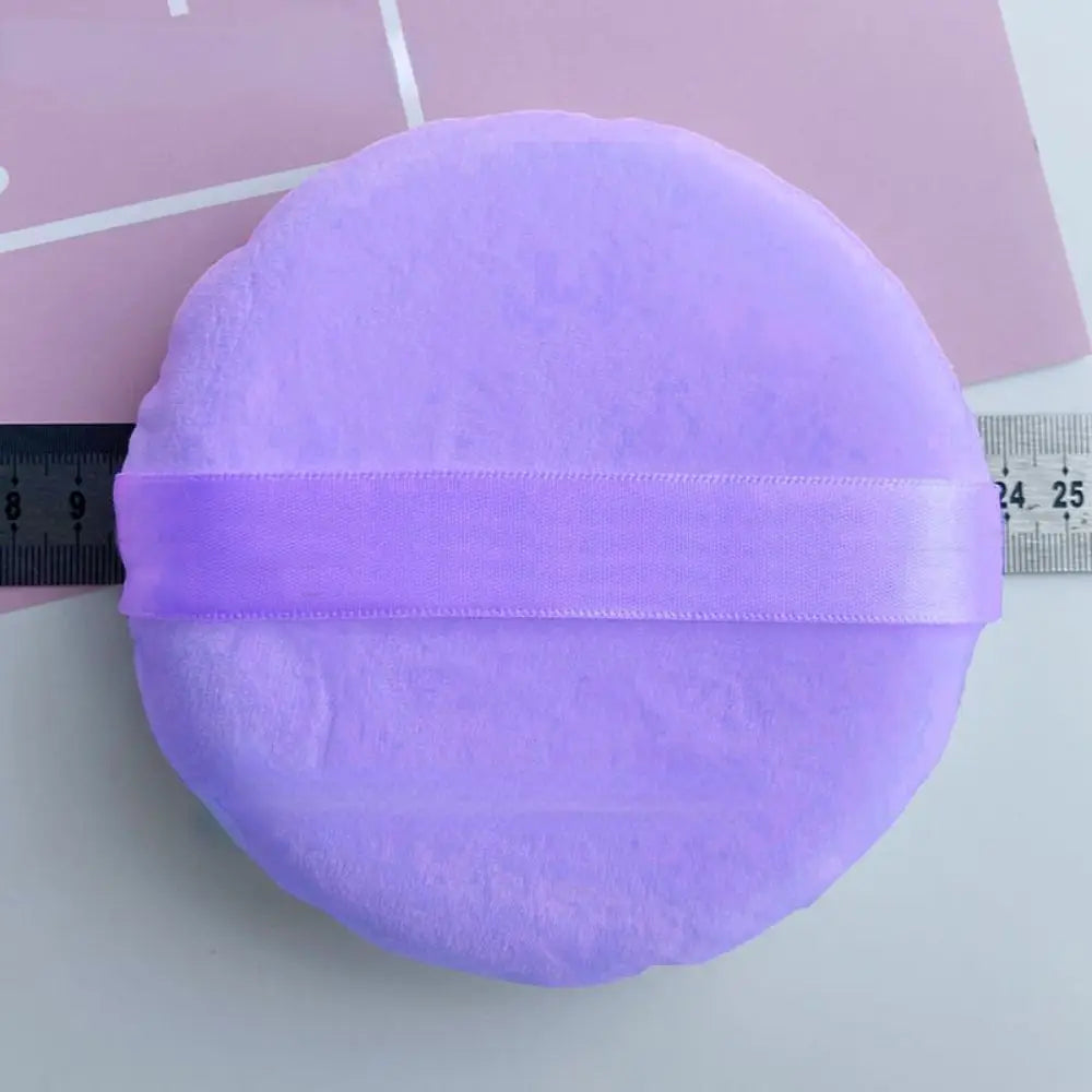 A purple jumbo soft powder puff with a lavender elastic band shown next to a ruler.