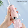 A hand holds a pink portable water flosser device, demonstrating its convenient and detachable design for dental cleaning.