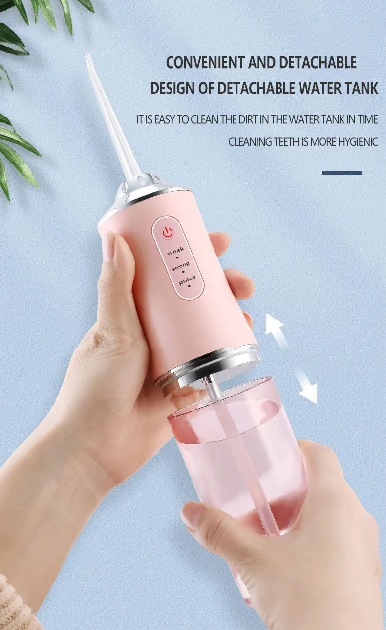 A hand holds a pink portable water flosser device, demonstrating its convenient and detachable design for dental cleaning.