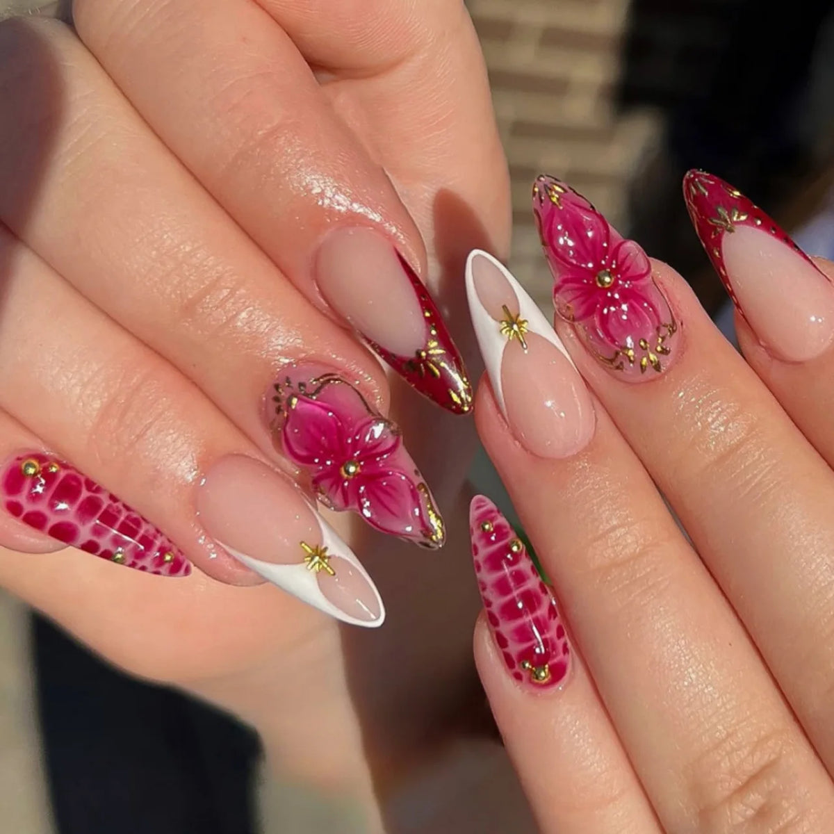 A close-up of hands displaying a set of 24 press-on nails featuring pink and magenta floral and butterfly designs.