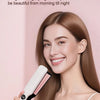 A woman is using a white ceramic hair straightener on her long brown hair in a bright pink setting.
