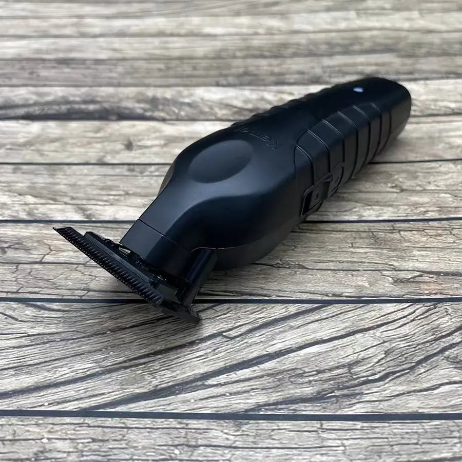 A black professional cordless electric hair clipper with a metal cutting comb resting on a weathered wooden surface.