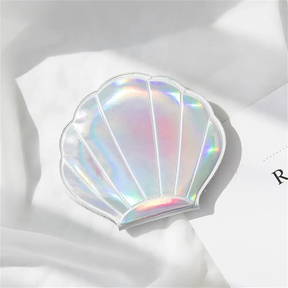 A iridescent, shell-shaped portable magnifying makeup mirror resting on a white surface.