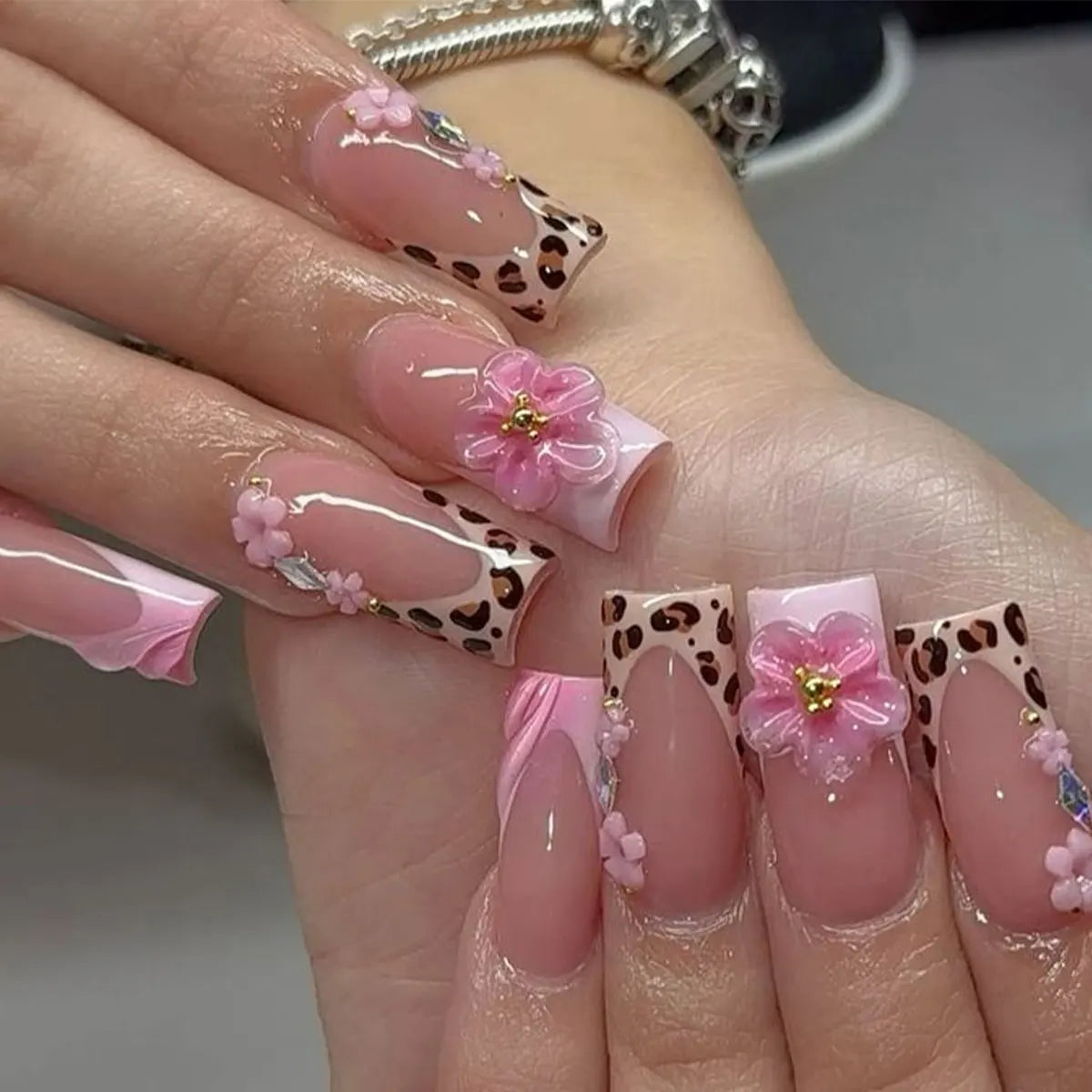 A hand displaying long pink nails with a leopard print design and small pink flowers.