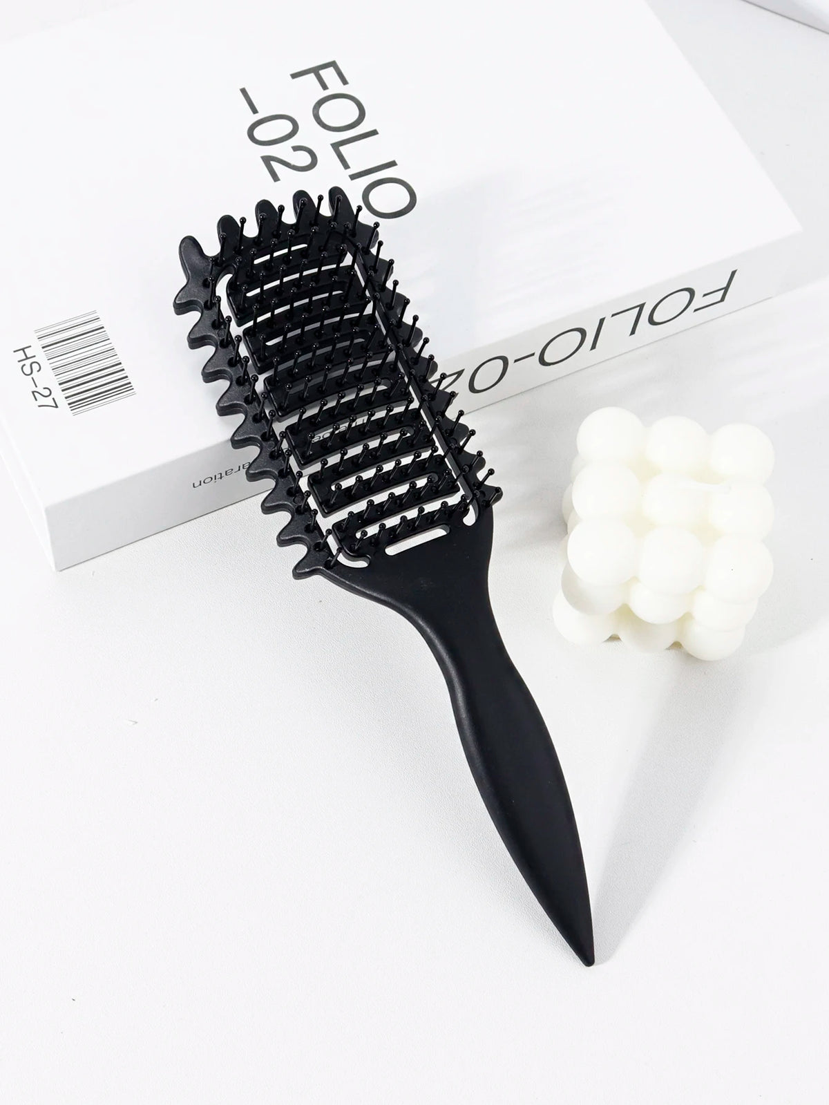 Peigne professionnel noir à cheveux bouclés avec dents posé sur une boîte blanche.