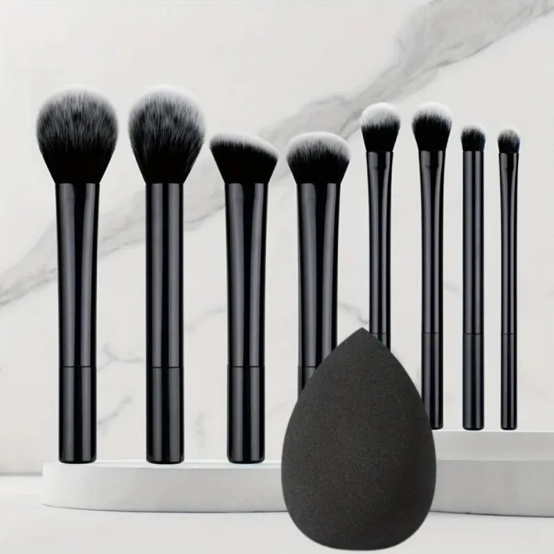 A set of nine black makeup brushes displayed vertically on a white surface with a large black brush head in the foreground.