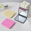 A set of pink and yellow portable makeup mirrors and a glass candle are displayed on a white surface.