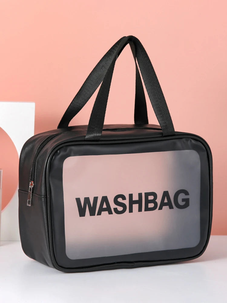 A black cosmetic storage bag with a clear window displaying the word WASHBAG against a pink background.