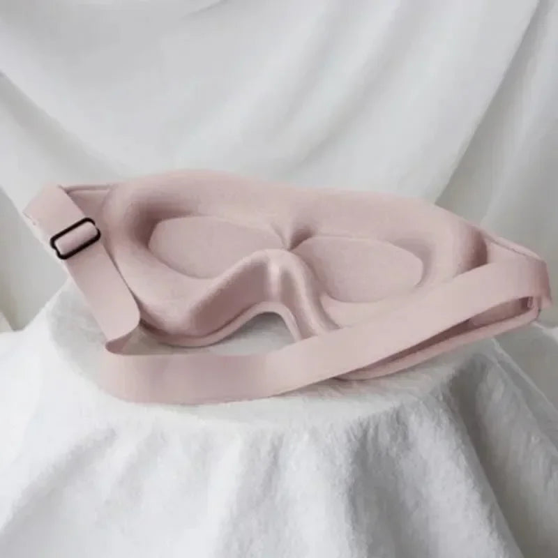 A light pink comfortable 3D sleeping eye mask is displayed on a white fabric background.