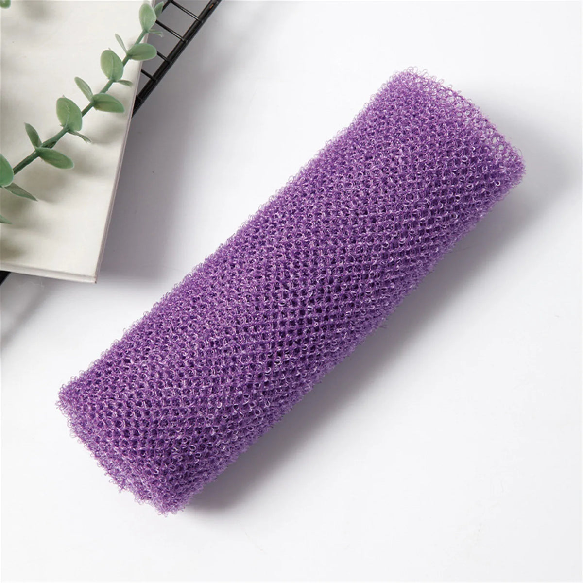 A purple reusable exfoliating bath sponge washcloth rolled up on a white surface.