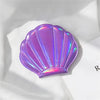 A purple iridescent seashell-shaped portable magnifying makeup mirror resting on a white surface.