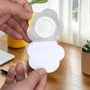 A hand is placing a white adhesive belly button patch onto a gray and yellow disposable castor oil patch.