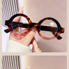 A pair of tortoiseshell round acetate reading glasses with pink lenses being held by a hand.
