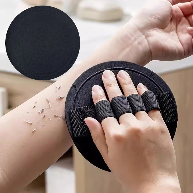 A hand is holding a black natural PVA body scrubbing shower brush with a circular cleaning pad.
