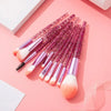 A set of ten long, pink glitter makeup brushes displayed on a pink background.