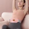 A woman is wearing a pink heated abdominal massage belt while relaxing on a sofa.