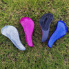 Four brightly colored detangling hair brushes—silver, pink, black, and blue—lie on green grass.