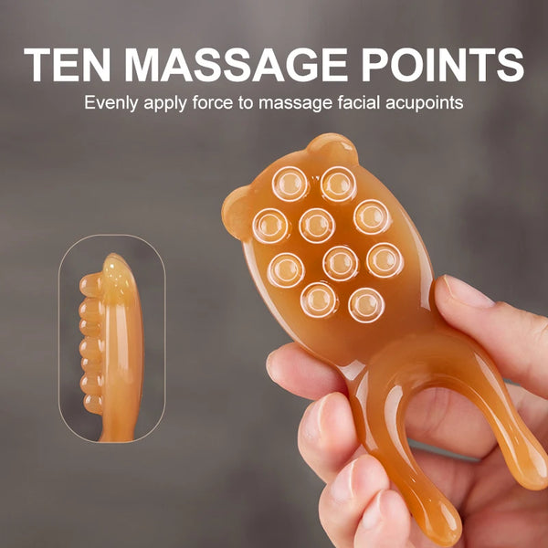 A hand holds an amber-colored facial massage tool with ten massage points for applying even force to acupoints.