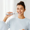 A woman is effortlessly cleaning her teeth at home using a smart ultrasonic dental cleaning device.