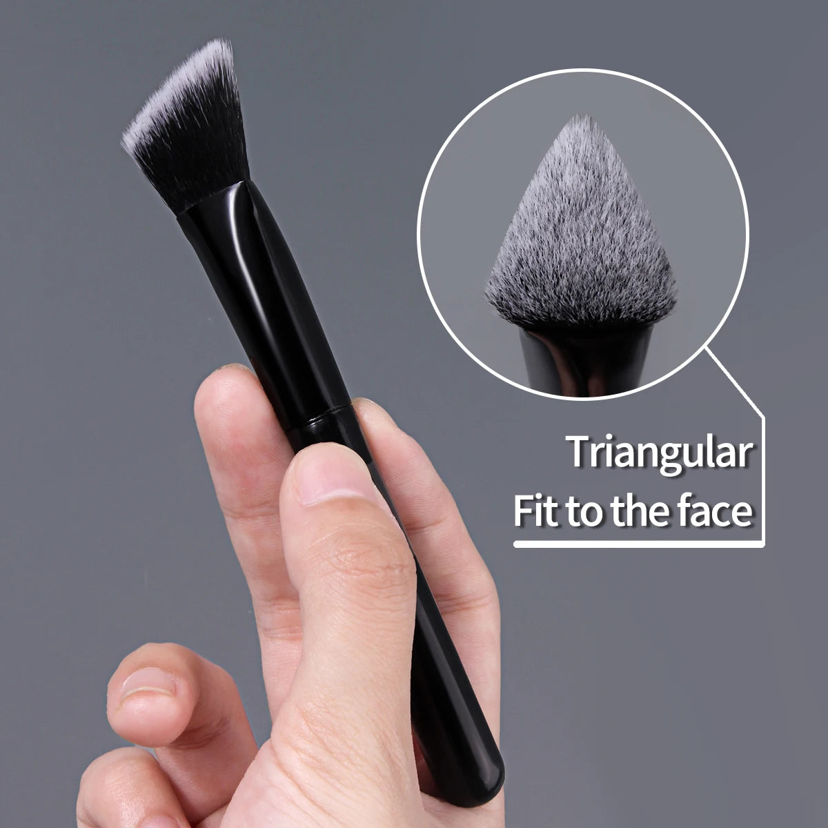 A hand holds a black triangular precision concealer brush, showing a magnified view of the brush head.