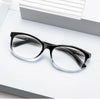 Une paire de lunettes de lecture à monture noire et verres clairs posée sur une surface blanche.