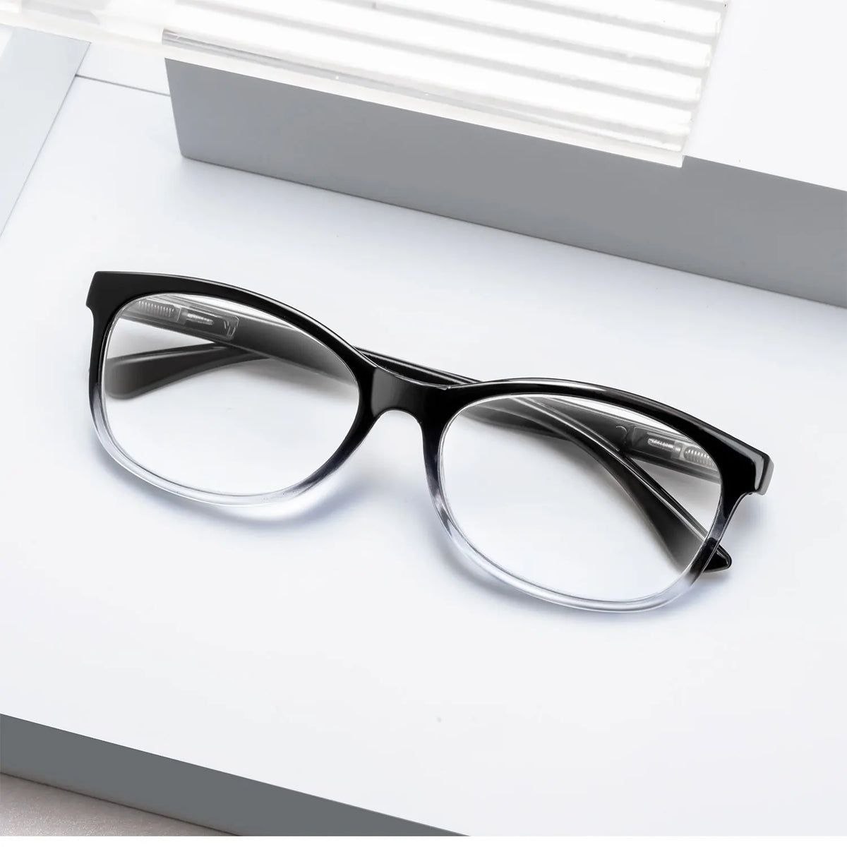 Une paire de lunettes de lecture à monture noire et verres clairs posée sur une surface blanche.