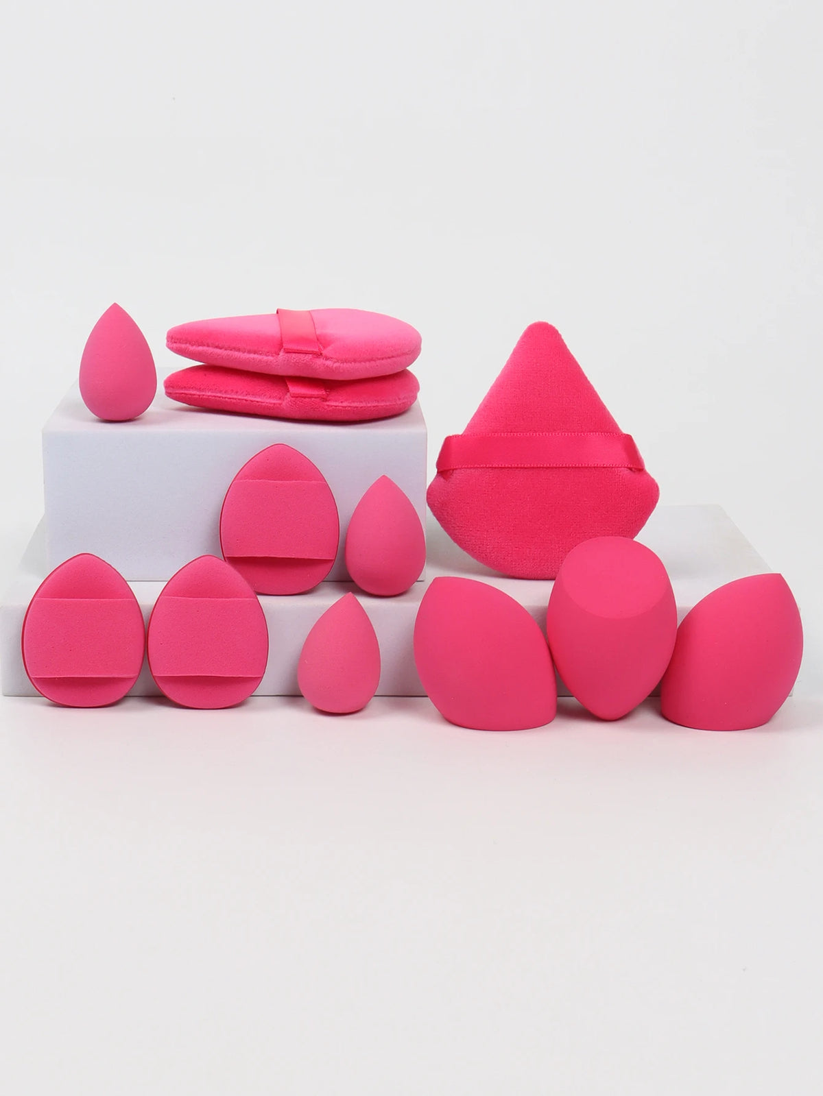 A collection of 12 pink makeup sponges arranged on a white surface.
