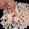 Colección de 120 uñas postizas en tonos nude y rosa pálido sobre una superficie oscura.