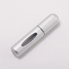 A silver portable refillable perfume bottle with a clear glass insert, shown in a profile view.