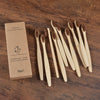 A set of ten natural bamboo toothbrushes is displayed next to its packaging box on a wooden surface.