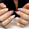 Primer plano de manos mostrando uñas pintadas con diseños florales en rosa, blanco y azul con detalles de mariquitas.