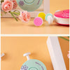 A light green electric baby nail trimmer with a flower design and various attachments is shown on a wooden surface.