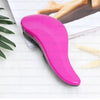 A bright pink classic detangling hair brush lying on a white surface next to a sheet of paper and some light-colored bristles