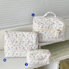 Three quilted white cotton makeup bags of different sizes are displayed on a white surface.