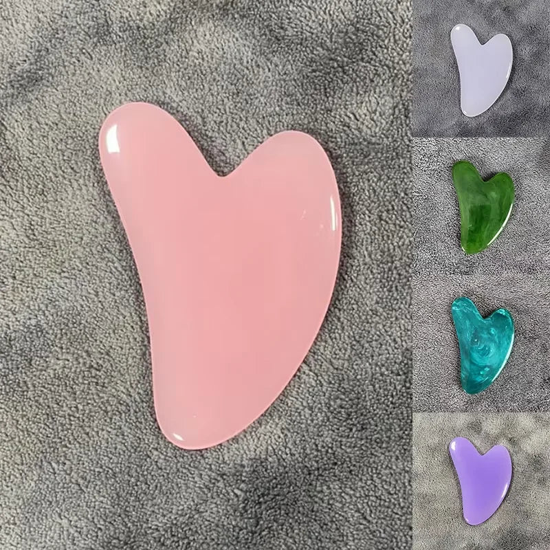 Masajeador facial de cera en forma de corazón rosa sobre tela gris texturizada con otros corazones de colores.