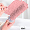 A hand is holding a pink silicone heat resistant mat for hair styling tools, showing its textured surface.