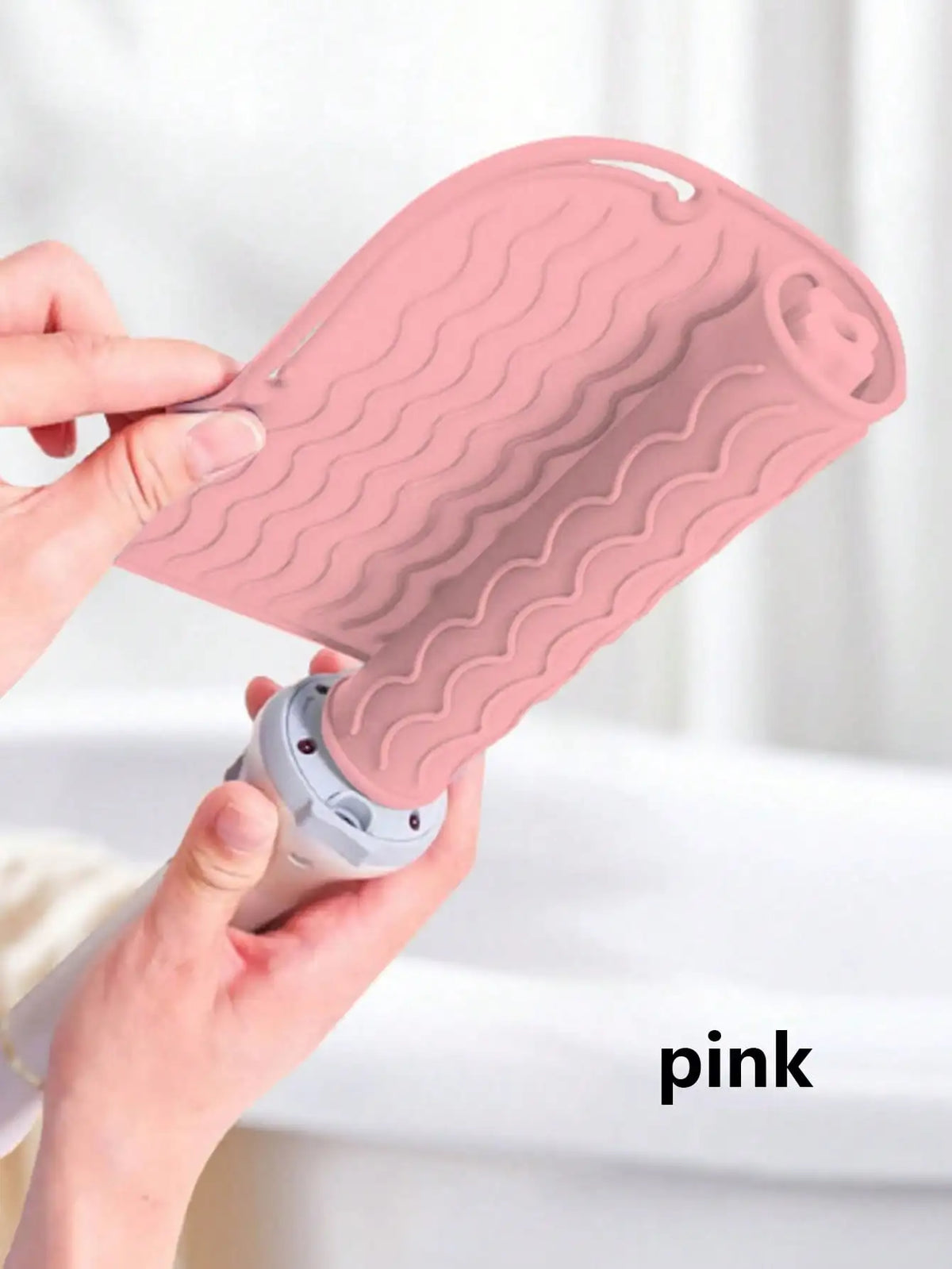 A hand is holding a pink silicone heat resistant mat for hair styling tools, showing its textured surface.