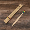 A bamboo toothbrush with soft bristles is shown lying on a wooden surface.