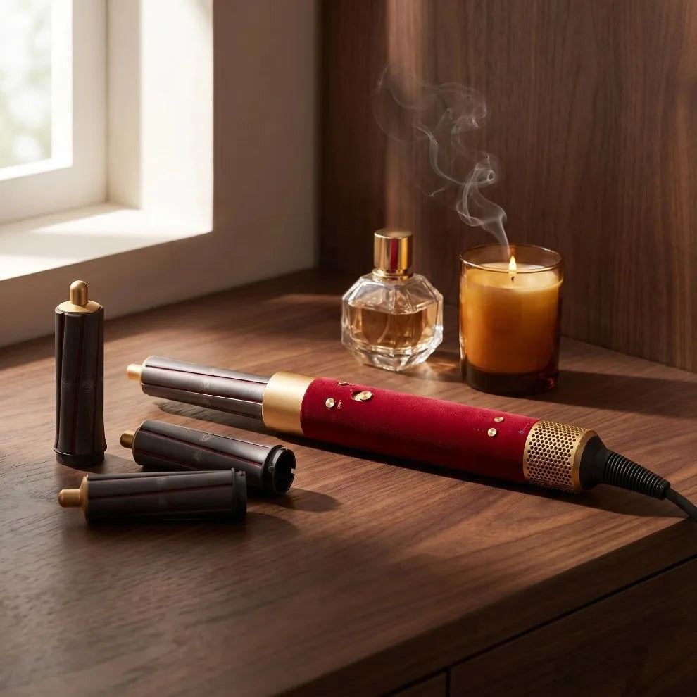 A wooden hair styling tool with a red handle and gold accents rests on a dark wood surface next to an amber glass and smoke.