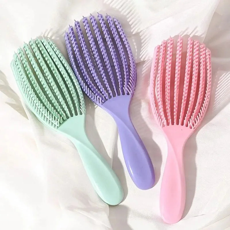 Three plastic hair brushes in shades of green, purple, and pink are displayed on a white background.
