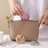 A hand places a pink rose-shaped makeup mirror onto a beige double-sided pocket makeup mirror.