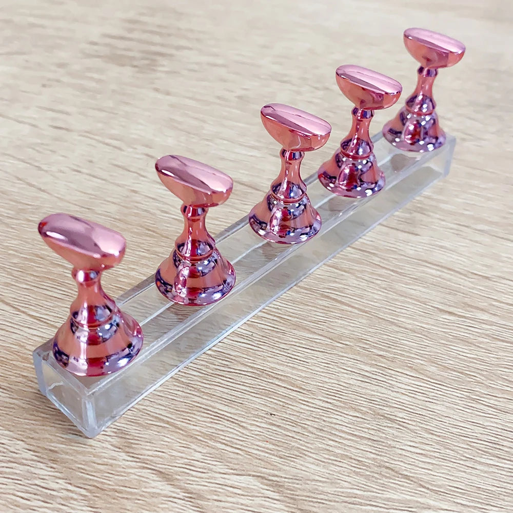 Un ensemble de supports à ongles magnétiques roses métalliques alignés sur un présentoir en acrylique transparent.