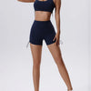 Una mujer modela un conjunto deportivo de yoga y gimnasio top y shorts azul marino transpirable y de secado rápido.
