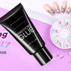 A black tube of Super Strong Rhinestone Glue for nail art is displayed next to loose rhinestones and pink flowers.