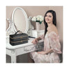 A woman sits next to a white vanity table with a silver mirror and a black PU leather hair dryer storage bag.