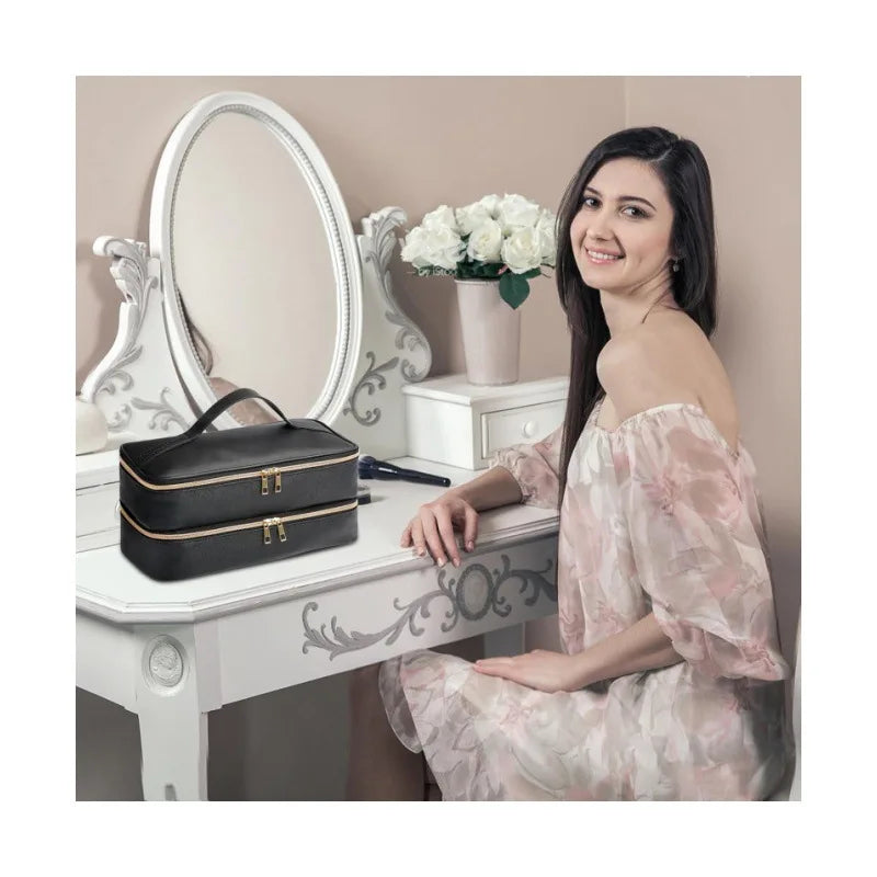 A woman sits next to a white vanity table with a silver mirror and a black PU leather hair dryer storage bag.