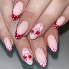 A close-up of a hand displaying press-on false nails with a sheer pink base and red polka dots and ladybug accents.