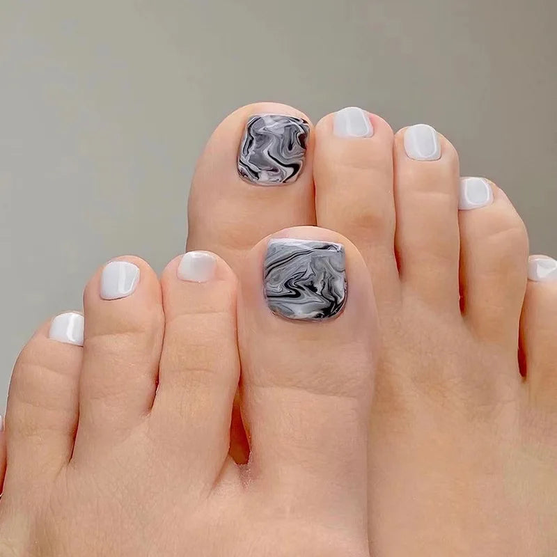 Nahaufnahme eines Fußes mit Nägeln, die mit schwarz-weiß marmoriertem Design lackiert sind.