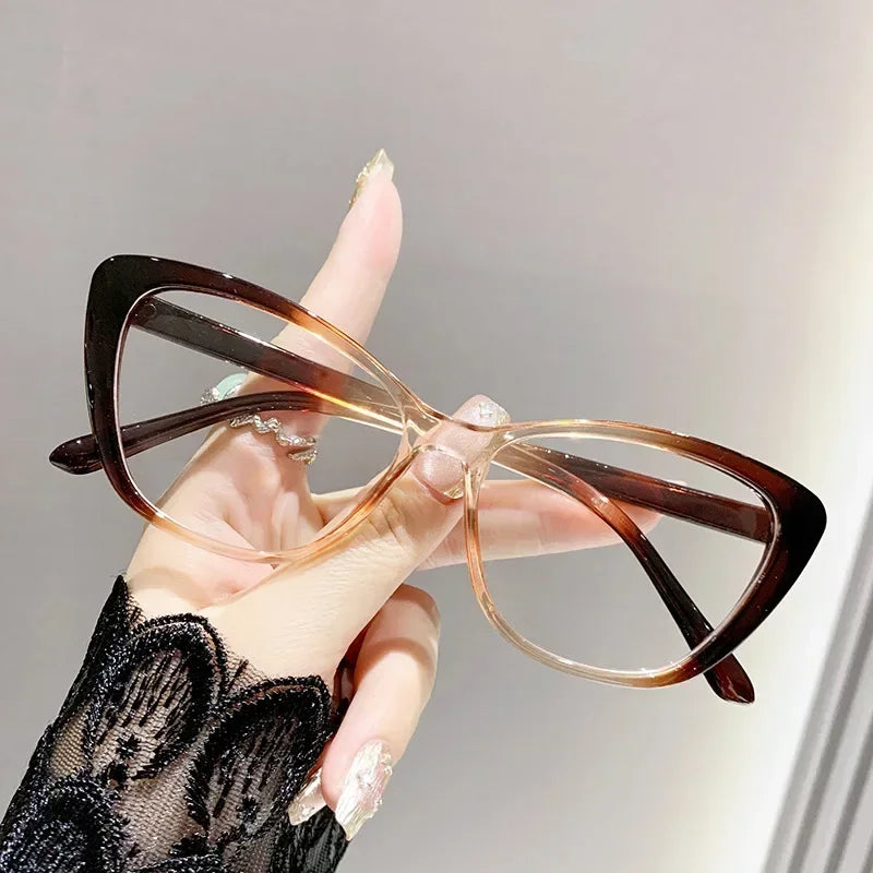 A hand holds a pair of elegant brown-framed cat eye reading glasses against a light gray background.