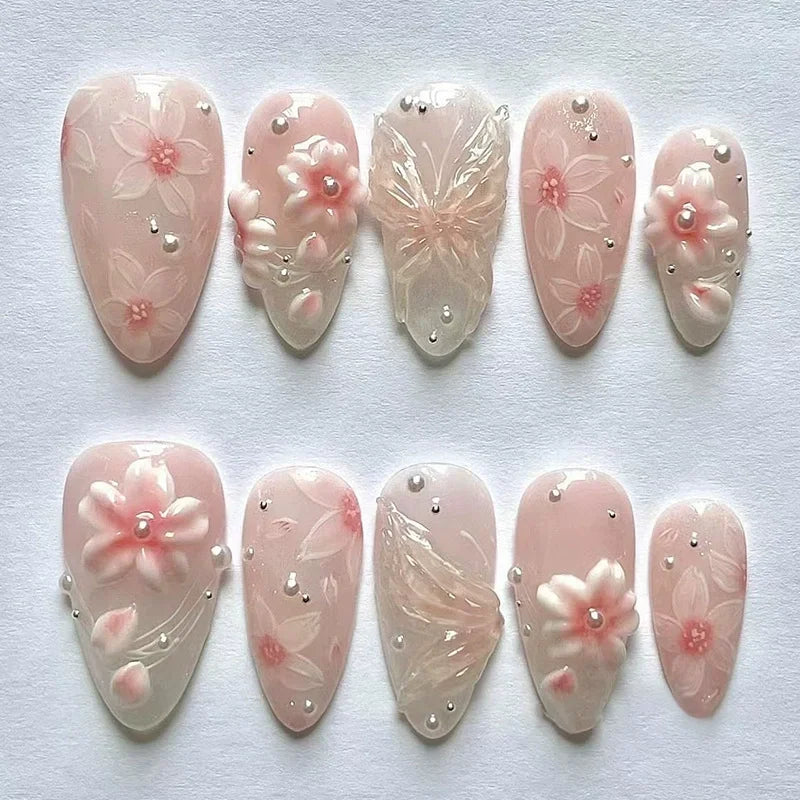 A collection of 24 press-on nails featuring delicate pink flowers and floral designs on a sheer pink background.
